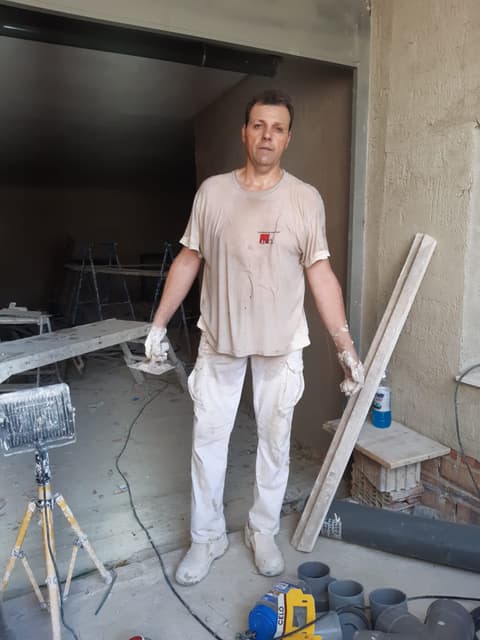 Yesista de Rafael Maderas S.L. en plena obra, con la ropa y los guantes manchados de yeso y una regla de madera apoyada a su lado