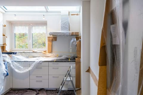 Cocina en plena reforma con los muebles cubiertos con plástico, protecciones de cartón y una escalera de tijera